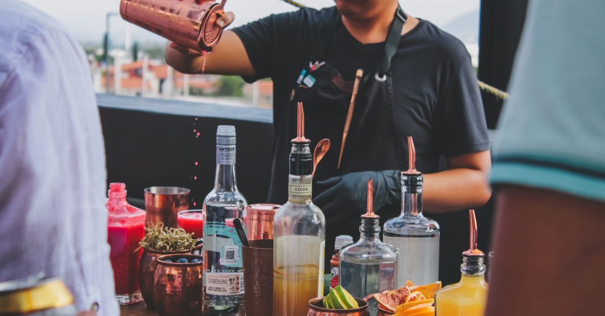 A bartender expertly pours drinks at an outdoor bar with colorful cocktail ingredients.